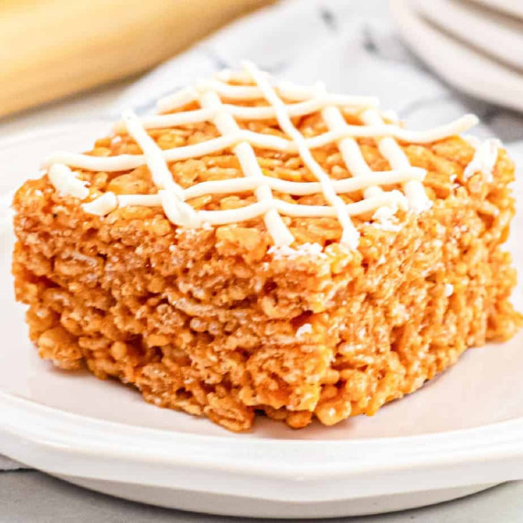 Orange pumpkin rice krispie treat at an angle on a plate close up topped with white chocolate.