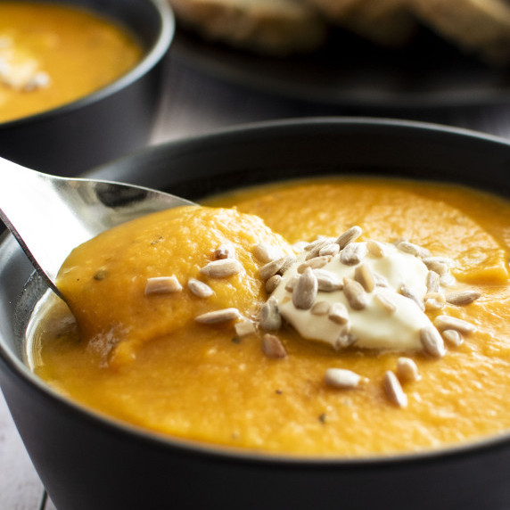 A spoon of pumpkin, sundried tomato & lentil soup being lifted out of a bowl.