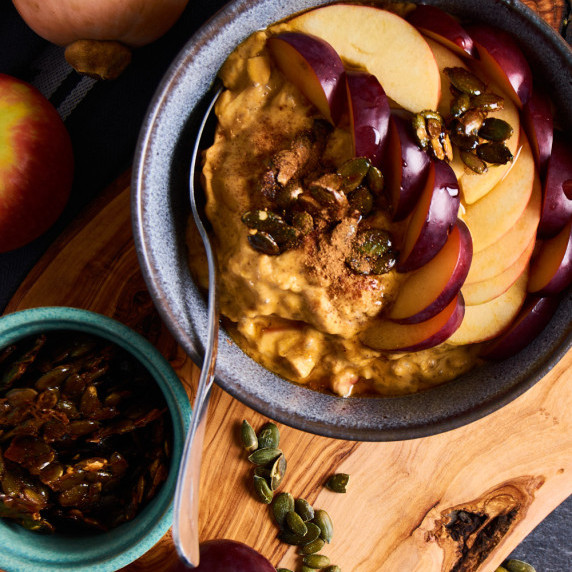 A blue bowl filled with Pumpkin Protein Oatmeal with Apple and Salted Caramel Pumpkin Seeds