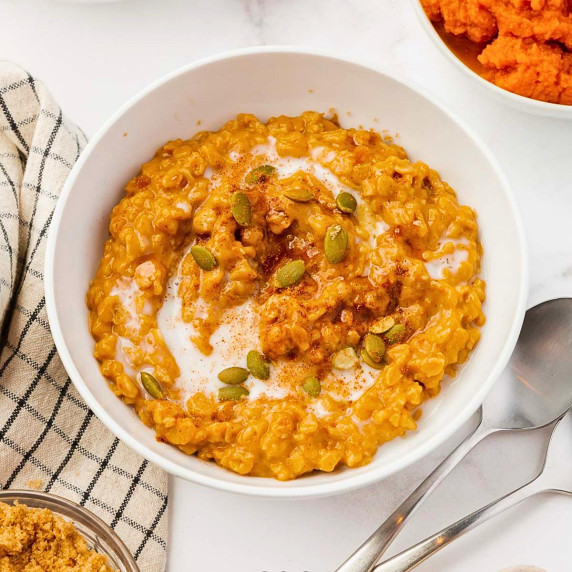 pumpkin oatmeal topped with pepitas, milk, brown sugar, and pumpkin pie spice in a white bowl