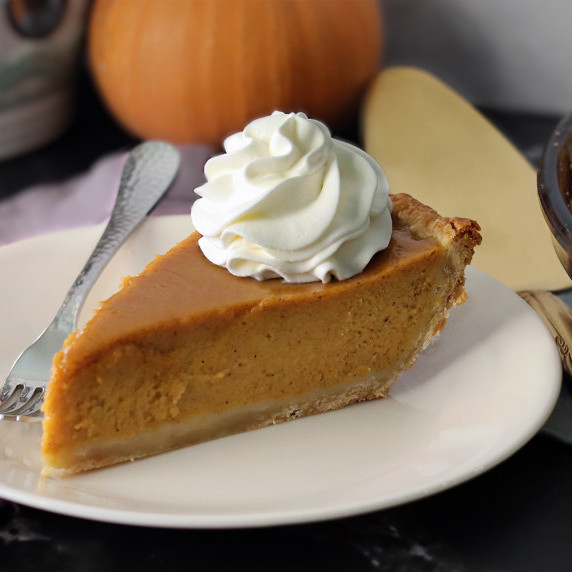 A slice of pumpkin pie on a white plate topped with whipped cream.