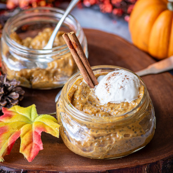 An autumn table scene with a seving of pumpkin chia pudding in a  glass container.