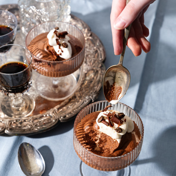 A hand holding a spoon to take a spoonful of chocolate mousse from a glass