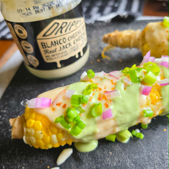 Smothered cob corn with a jar of white queso in the background.