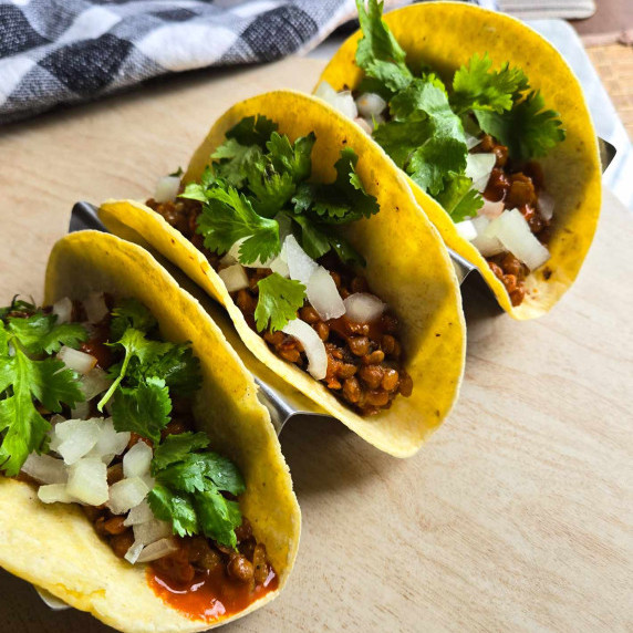 3 yellow corn tortillas filled with spicy lentils, white onions, and green cilantro.