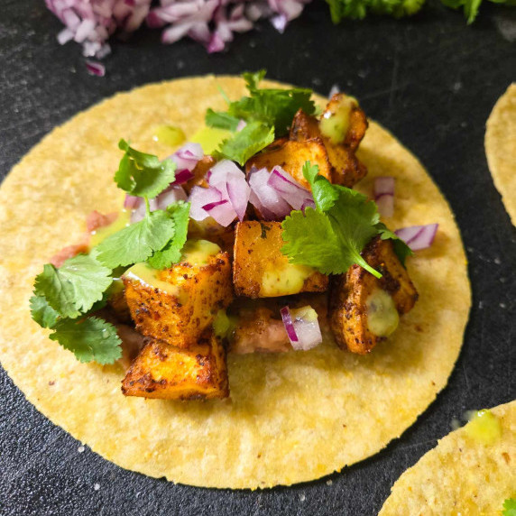 A yellow corn tortilla topped with potatoes, red onions, and green cilantro