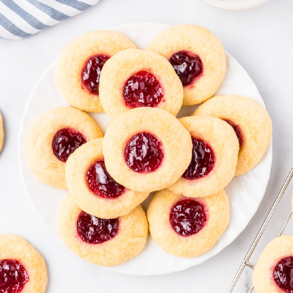 Raspberry thumbprint cookies on a plate from above with a wire cooling rack with more cookies nearby
