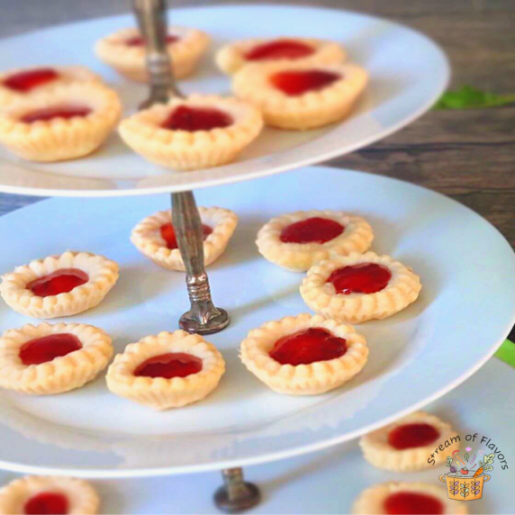 Raspberry jam tarts on a white dessert stand on a wooden background with a napkin and fresh berries