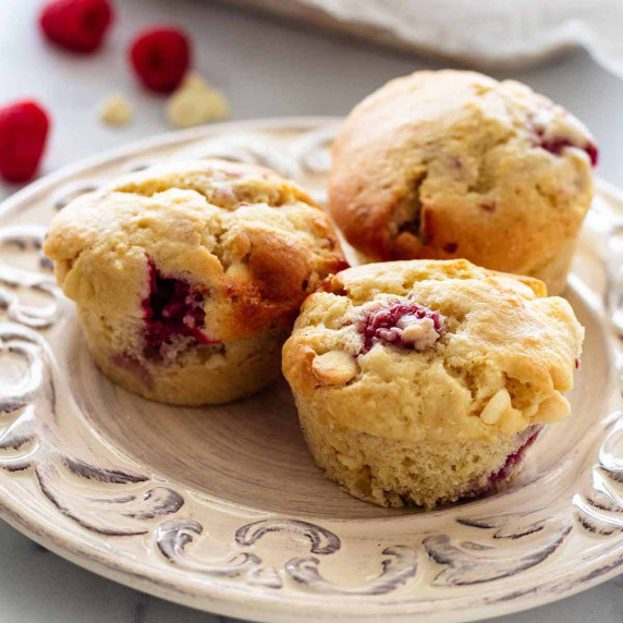 Three raspberry and white chocolate muffins on a white plate