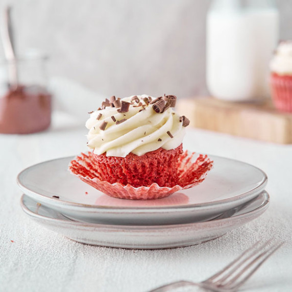 Single red velvet cupcake with cream cheese frosting sitting on a plate 