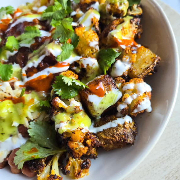 A colourful bowl of roasted cauliflower and potatoes dressed in colourful salsas & green cilantro