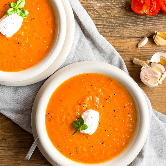 Raosted Tomato and Garlic soup in an off-white bowl with a coconut cream & fresh basil garnish.