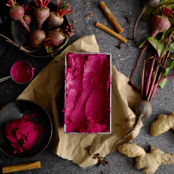 Red beet gingerbread ice cream in a loaf pan on a grey surface. 
