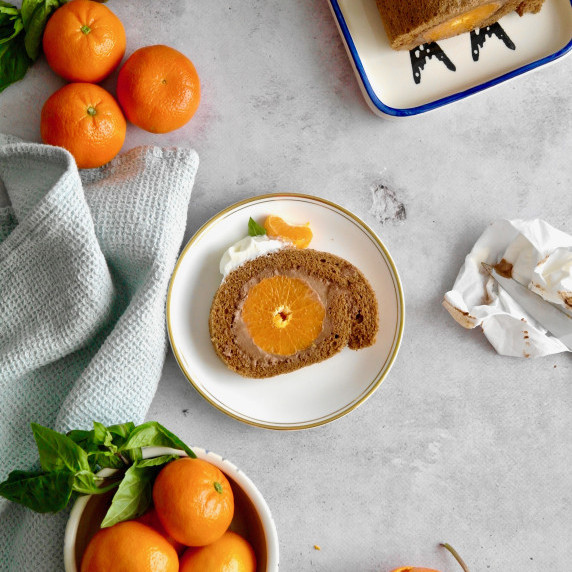 Slice of chocolate and mandarin orange roll cake on a white plate on a grey concrete surface. 