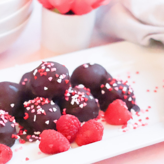 chocolate raspberry cheesecake truffles on a white tray with sprinkles and fresh raspberries