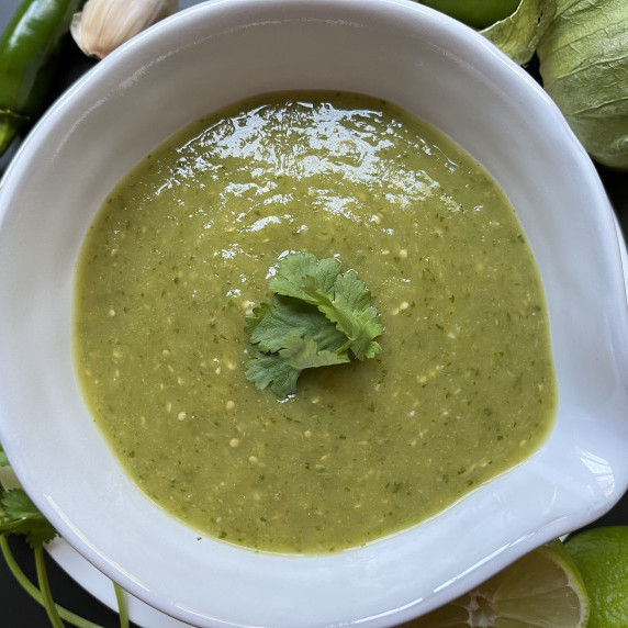 Salsa verde in a white bowl garnished with fresh cilantro leaves on a black countertop.