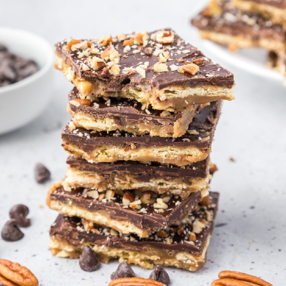 A stack of chocolate saltine toffee bars with pecans on top and the top piece missing a bite.
