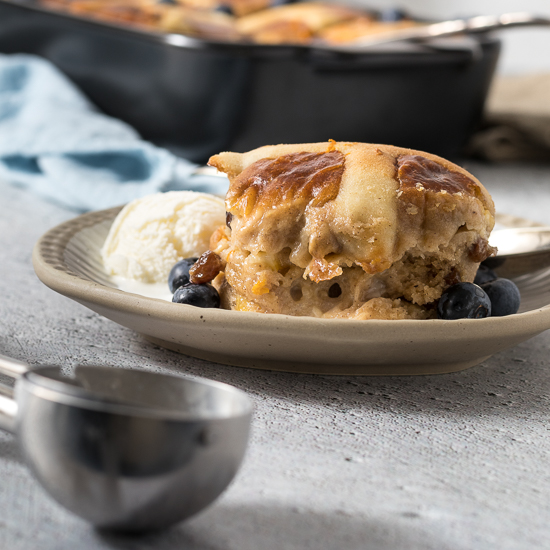 Hot cross bun pudding on a plate with ice cream and fresh blueberries.