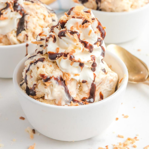 A bowl of Samoa ice cream topped with whipped cream, chocolate syrup, and crunchy coconut.