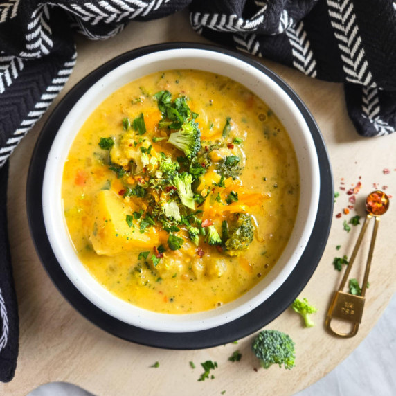 A white bowl full of orange hued soup with a black towel and plate in the background.