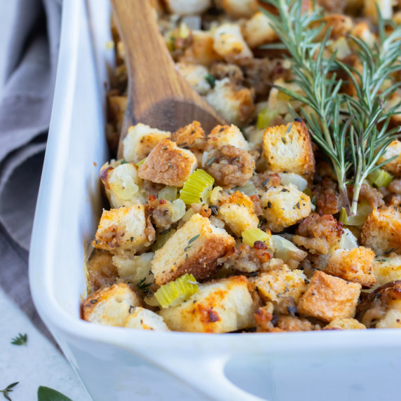 Sausage Stuffing RECIPE in a white casserole dish with a wooden serving spoon.