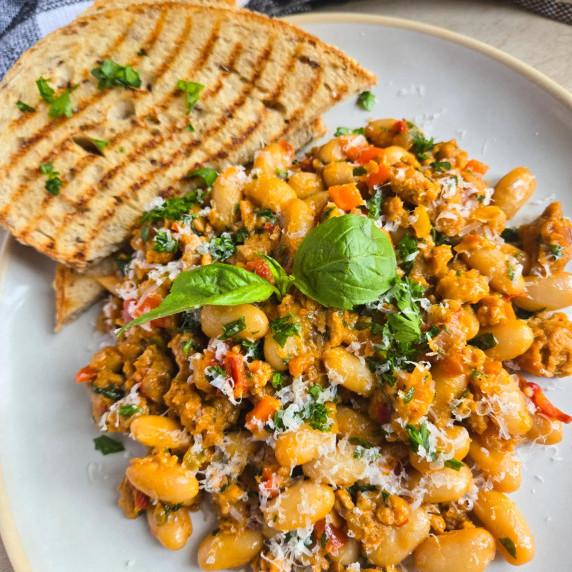 A colourful pile of beans and sausage with green herbs and golden, grilled bread.