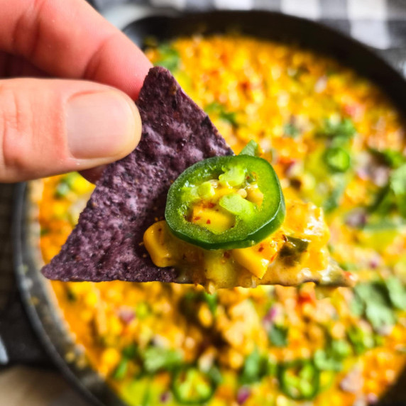 Blue corn tortilla chip smothered in golden corn queso and topped with a green jalapeno