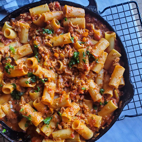 A skillet full of rigatoni pasta tossed in a rosy coloured sausage sauce.