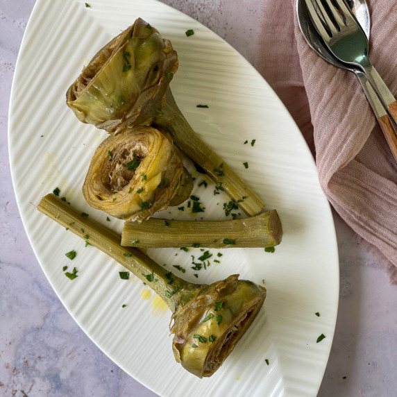 Sautéed Artichokes on a white plate, with serving fork and spoon.