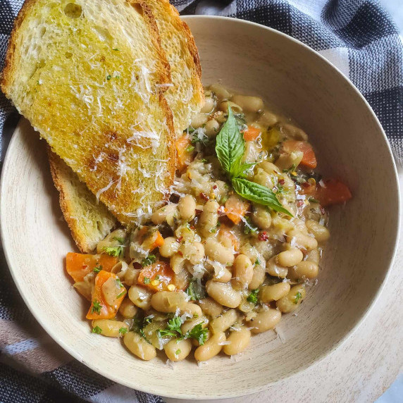 A wood bowl filled with savoury beans, golden toast, and pops of green herbs.