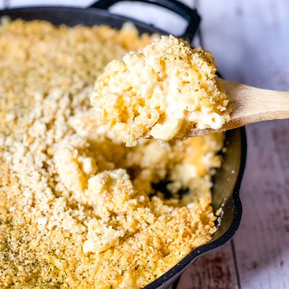 Smoked macaroni and cheese in a cast iron skillet being scooped up with a wooden spoon.
