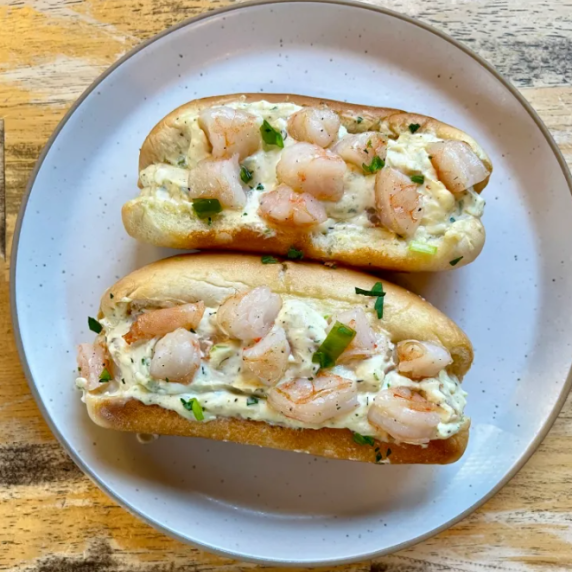 Two warm shrimp rolls on a white plate on a wooden table