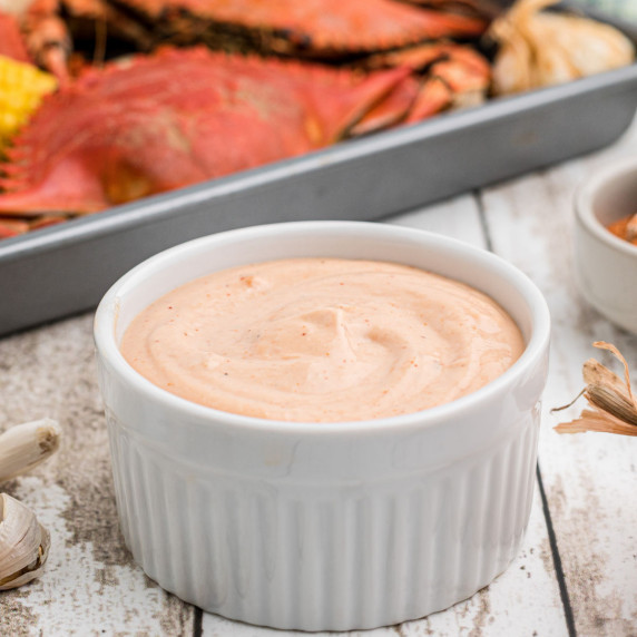 a large bowl of seafood sauce in a white ramekin with some boiled crabs in the background