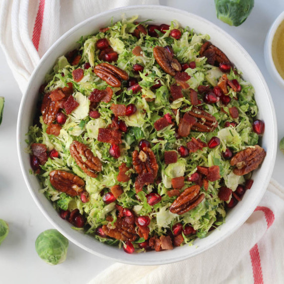 shaved Brussels sprouts salad with crumbled bacon in white bowl on white countertop