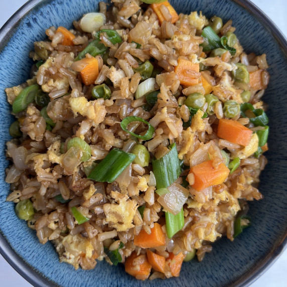 Fried brown rice with carrots, green peas, egg, and onion served in a blue bowl.