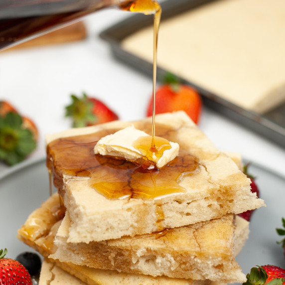 stack of sheetpan pancakes with a pat of butter and syrup being poured on top
