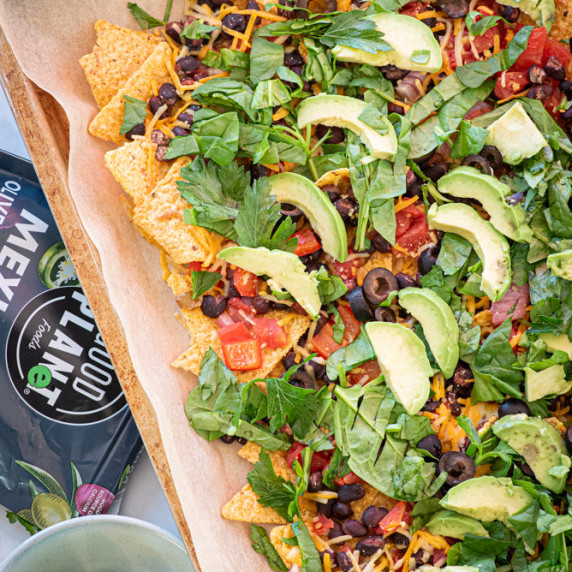 A pan of baked nachos topped with fresh vegetables