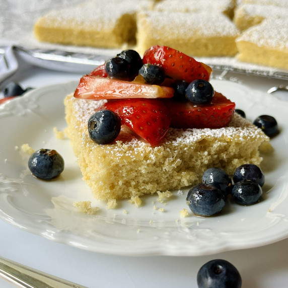 Slice of shortcake on a white plate topped with blueberries and sliced strawberries.