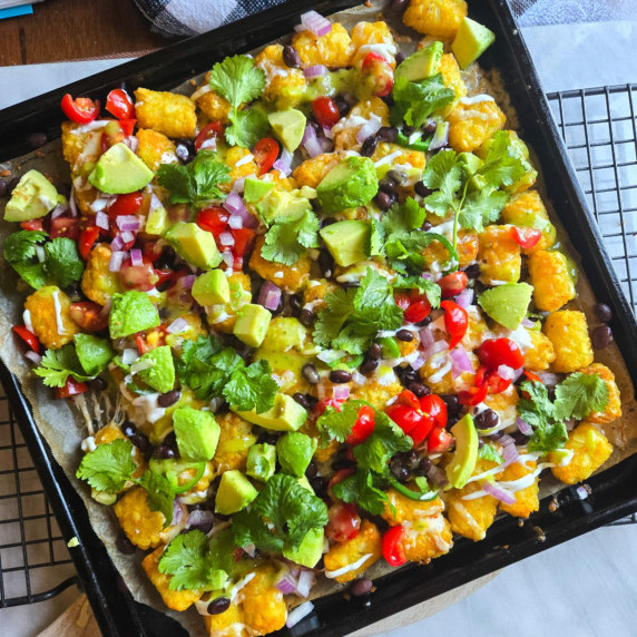 A tray of golden tater tots topped with a colourful assortment of garnishes