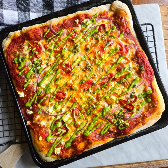 Pizza topped with melty cheese and a green drizzle of fresh pesto.