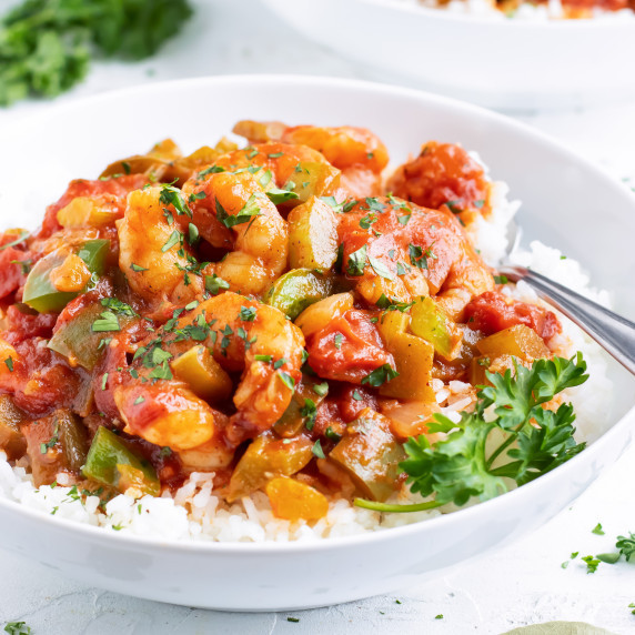 Shrimp Creole RECIPE served in a white bowl over rice and garnished in greens.