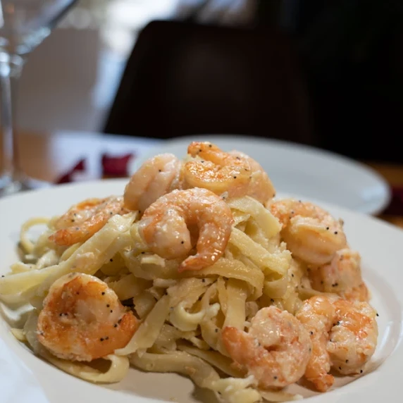 A white plate with pasta noodles, shrimp, and fettuccine alfredo sauce.