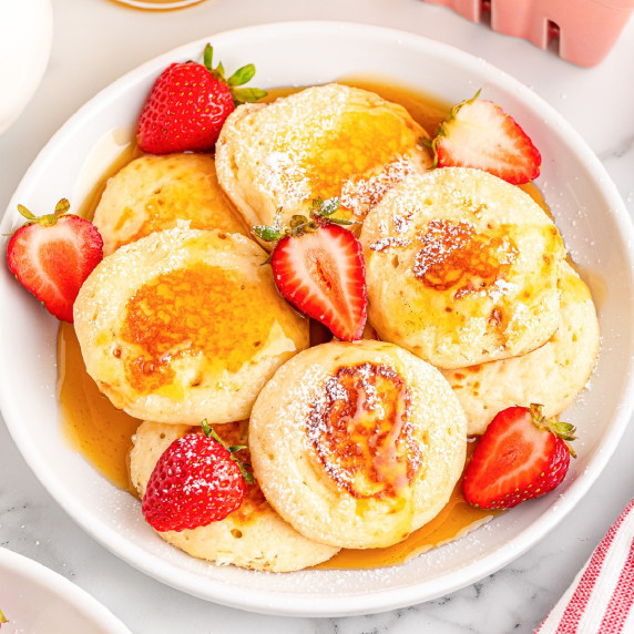 A plate of silver dollar pancakes with fresh strawberries and maple syrup.
