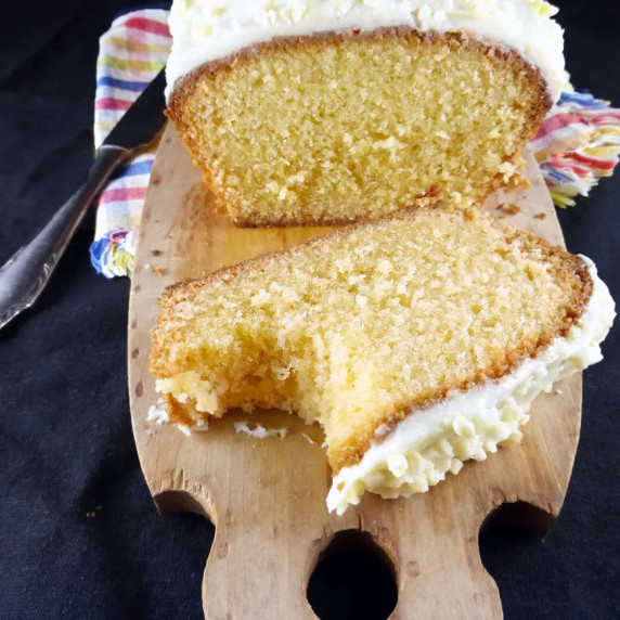 front view of a madeira loaf cake with a cut slice on a wooden board