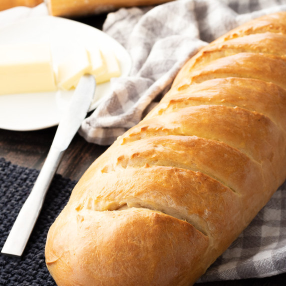 Baked soft french bread on towel with plate of butter and knife. 