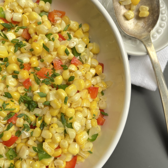 Sauteed fresh corn, red and green pepper and onions garnished with chives in a white bowl.