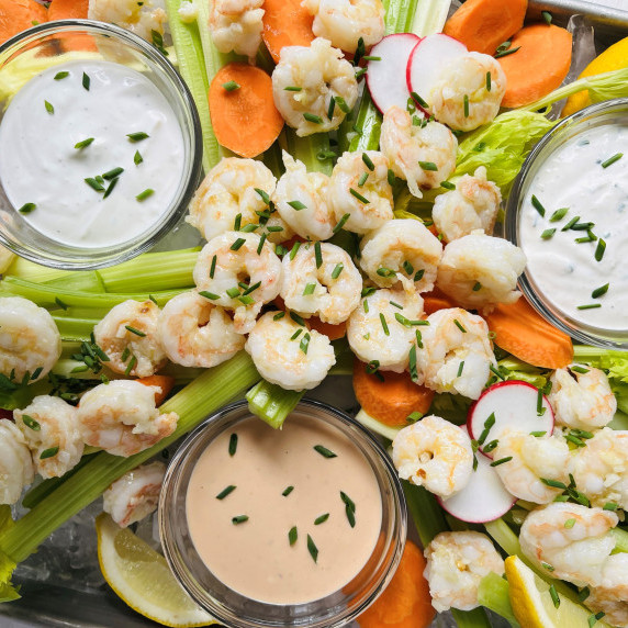 Sautéed shrimp on a platter with dipping sauces, celery sticks, sliced carrots and radishes.