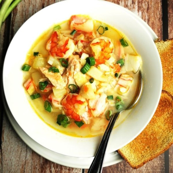 seafood soup poured into white bowl with toast on the side