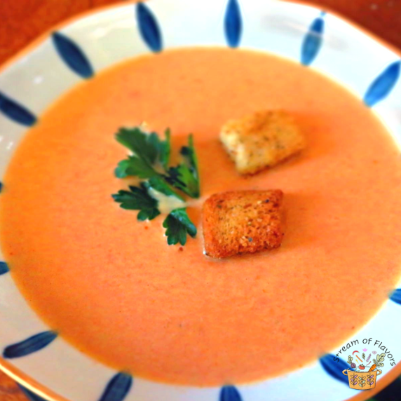 Tomato soup in a white and blue bowl with croutons and parsley