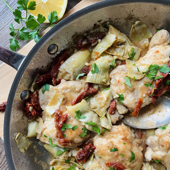 Chicken thighs, artichokes and sun-dried tomatoes in a skillet.